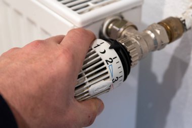 Male hand turns a radiator thermostat. High quality photo clipart