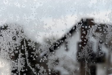 Çok güzel donmuş bir pencerenin detaylı bir yakın görüntüsü karmaşık desenler sergiliyor ve arka planda muhteşem bir dağ görünüyor.