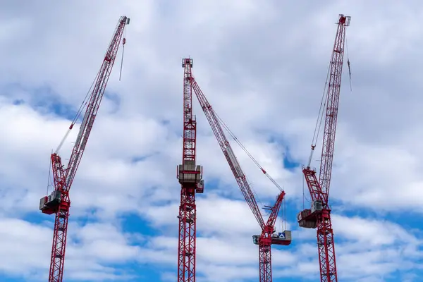 Bir dizi çarpıcı kırmızı ve beyaz vinç bulutlu mavi gökyüzünün zeminine karşı dik duruyor ve dinamik bir görsel yaratıyor.