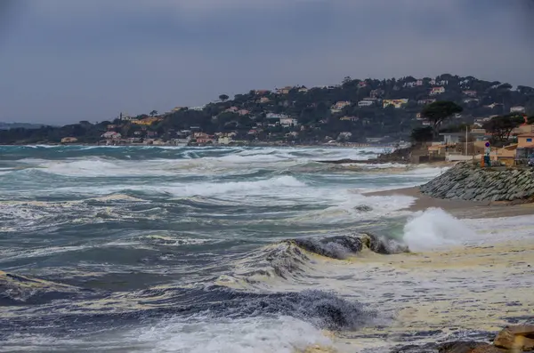 Güçlü dalgalar engebeli kayalık kıyı şeridine sert bir şekilde çarpıyor, karamsar ve bulutlu bir günde dramatik sıçramalar yaratıyor.