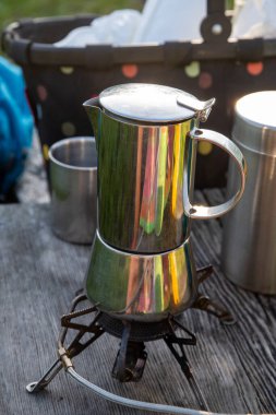 Güzel cilalanmış ahşap bir masanın üzerinde nefis bir fincan kahve demlemek için bekleyen parlak ve modern paslanmaz bir kahve makinesi var.