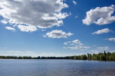 Güzel nehir manzarası. Güneşli bir günde göl yüzeyi. Suyun yüzeyi ağaçların arka planına ve mavi gökyüzüne karşı. Bulanık resim, seçici odak