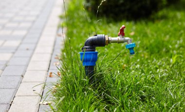 Parkın bahçesindeki yeşil çimleri sulamak için su hortumunu ayarlayan musluk. Doğanın arka planında krom su kaynağı