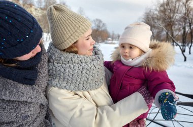 Büyükanne, anne ve kız Noel ve yeni yıl tatillerinde kış şehir parkında yürüyorlar. Ebeveyn ve küçük çocuk dışarıda eğleniyor.