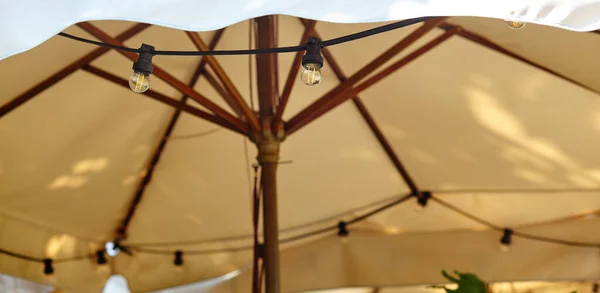 Restoran terası şemsiyesi ve ampuller. Kafe akşam aydınlatması için ekipman. Bulanık resim, seçici odak