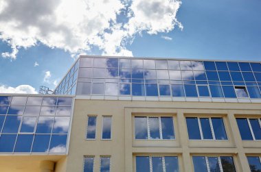 Bulutlar modern ofis binasının camlarına yansıyor. Güneşli bir günde, mavi gökyüzü olan modern binanın dışı.