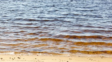 Kıyının kenarında su var. Kumlu sahilde mavi deniz dalgası. Sahilde su dalgaları olan güzel bir arka plan.