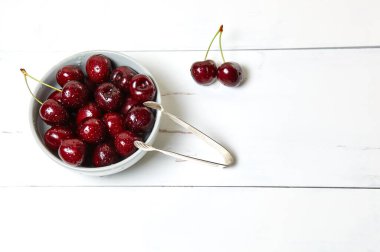 Ahşap arka planda seramik bir kasede tatlı kirazlar, yakın plan. Bir kase dolusu su damlacıkları olan taze kirazlar.