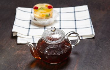 Çaydanlıkta siyah çay ve ahşap zemin üzerinde reçelli kek. Lezzetli mini tatlı ve kahvaltıda geleneksel çay, yakın plan.