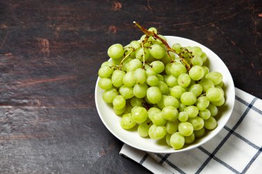 Tabakta su damlaları olan olgun yeşil üzüm dalı. Tahta arka planda sulu üzümler, yakın plan. Fotokopi alanı olan koyu mutfak masasında üzümler