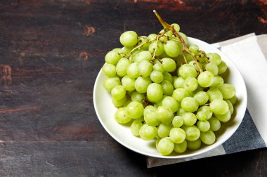 Tabakta su damlaları olan olgun yeşil üzüm dalı. Tahta arka planda sulu üzümler, yakın plan. Fotokopi alanı olan koyu mutfak masasında üzümler