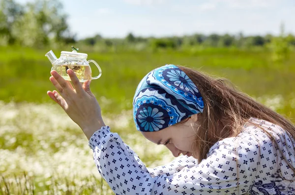 stock image Woman holding transparent teapot with herbal tea. Collects fresh green herbs harvest and make healthy tea. Blurred image, selective focus