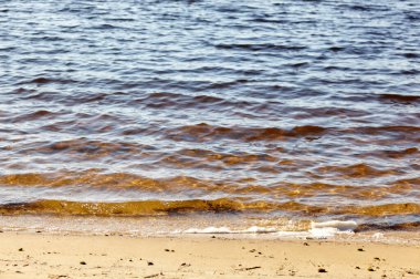 Kıyının kenarında su var. Kumlu sahilde mavi deniz dalgası. Sahilde su dalgaları olan güzel bir arka plan.