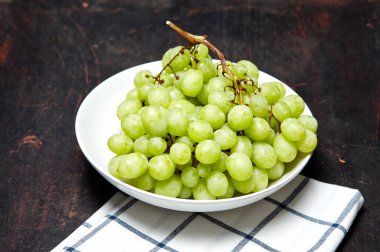Tabakta su damlaları olan olgun yeşil üzüm dalı. Tahta arka planda sulu üzümler, yakın plan. Fotokopi alanı olan koyu mutfak masasında üzümler
