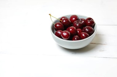 Ahşap arka planda seramik bir kasede tatlı kirazlar, yakın plan. Taze taze kirazlar bir kase içinde su damlacıkları