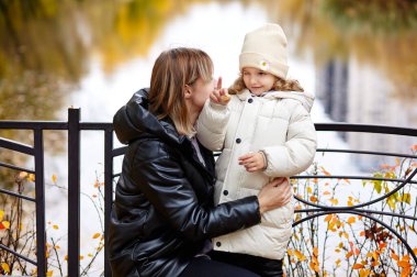 Merhaba Ekim. Anne ve kızı sonbahar şehir parkında yürüyorlar. Ebeveyn ve küçük çocuk dışarıda eğleniyor.