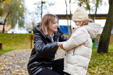 Merhaba Ekim. Anne ve kızı sonbahar şehir parkında yürüyorlar. Ebeveyn ve küçük çocuk dışarıda eğleniyor.
