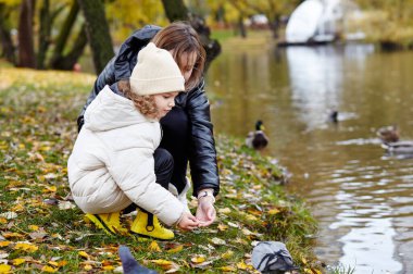 Merhaba Ekim. Anne ve kızı sonbahar şehir parkında yürüyorlar. Ebeveyn ve küçük çocuk dışarıda eğleniyor.