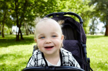 Bebek arabasında bir yaz parkında yürüyüş. Sevimli küçük kız sandalyede oturuyor ve gülümsüyor. Bebek arabasındaki çocuk