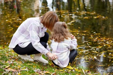 Merhaba Ekim. Anne ve kızı sonbahar şehir parkında yürüyorlar. Ebeveyn ve küçük çocuk dışarıda eğleniyor.