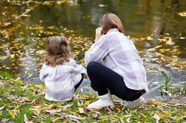 Merhaba Ekim. Anne ve kızı sonbahar şehir parkında yürüyorlar. Ebeveyn ve küçük çocuk dışarıda eğleniyor.