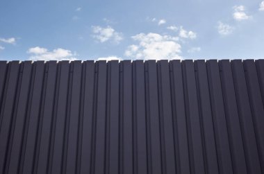 Mavi gökyüzüne karşı yontulmuş çelik çit. Oluklu metal doku yüzeyi veya çeliği galvanize et