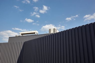 Oluklu demir levha çitleri, arka plan olarak bir depo veya fabrika endüstriyel binası ön cephesi. Mimarlık. Metal doku