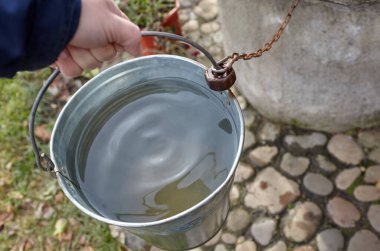 Metal kovayı taze suyla tutan bir adam. Kırsal bölgedeki derin bir kuyudan gelen su.