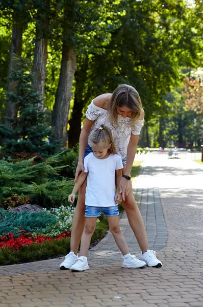 Anne ve kızı yazın şehir parkında yürürler. Çocukluk, eğlence ve insan konsepti - mutlu aile doğada dinlenir ve iyi vakit geçirir.