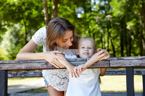 Anne ve kızı yazın şehir parkında yürürler. Çocukluk, eğlence ve insan konsepti - mutlu aile doğada dinlenir ve iyi vakit geçirir.
