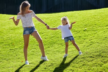 Anne ve kızı yaz parkında çimlerde yürüyor. Çocukluk, eğlence ve insan konsepti. Mutlu aile istirahatı ve iyi vakit geçirmek.