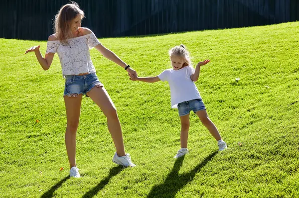 Anne ve kızı yaz parkında çimlerde yürüyor. Çocukluk, eğlence ve insan konsepti. Mutlu aile istirahatı ve iyi vakit geçirmek.