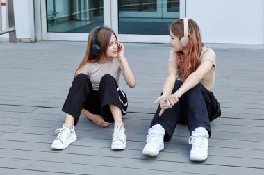 Alışveriş merkezinin yanında oturmuş müzik dinleyen iki genç kız arkadaş. Moda kıyafetleri içinde gülümseyen hippi kızlar. Mutlu kız arkadaşlar rahatlıyor ve iyi vakit geçiriyor.