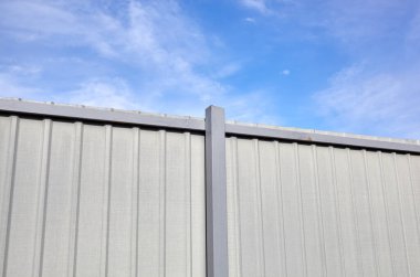 Mavi gökyüzüne karşı yontulmuş çelik çit. Oluklu metal doku yüzeyi veya çeliği galvanize et