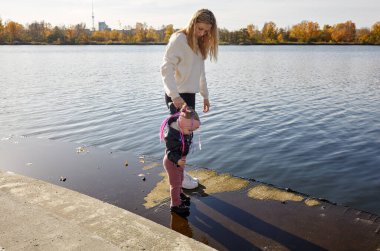Merhaba Ekim. Anne ve kızı sonbahar şehir parkında yürüyorlar. Ebeveyn ve küçük çocuk dışarıda eğleniyor.