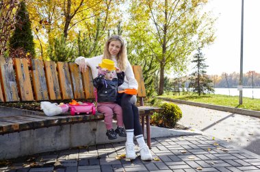 Merhaba Ekim. Anne ve kızı sonbahar şehir parkında yürüyorlar. Ebeveyn ve küçük çocuk dışarıda eğleniyor.