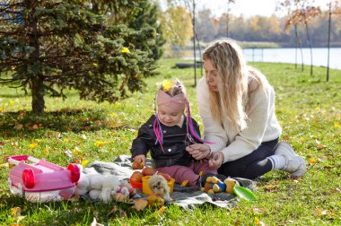 Merhaba Ekim. Anne ve kızı sonbahar şehir parkında yürüyorlar. Ebeveyn ve küçük çocuk dışarıda eğleniyor.