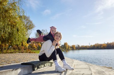 Merhaba Ekim. Anne ve kızı sonbahar şehir parkında yürüyorlar. Ebeveyn ve küçük çocuk dışarıda eğleniyor.