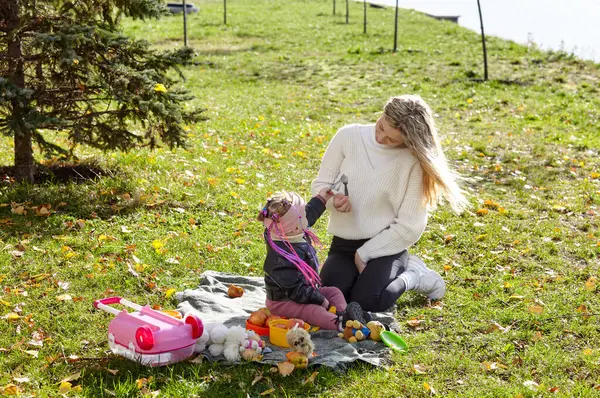 Merhaba Ekim. Anne ve kızı sonbahar şehir parkında yürüyorlar. Ebeveyn ve küçük çocuk dışarıda eğleniyor.