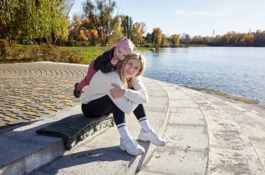 Merhaba Ekim. Anne ve kızı sonbahar şehir parkında yürüyorlar. Ebeveyn ve küçük çocuk dışarıda eğleniyor.