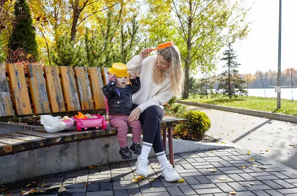 Merhaba Ekim. Anne ve kızı sonbahar şehir parkında yürüyorlar. Ebeveyn ve küçük çocuk dışarıda eğleniyor.