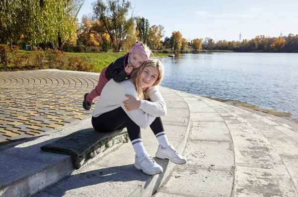 Merhaba Ekim. Anne ve kızı sonbahar şehir parkında yürüyorlar. Ebeveyn ve küçük çocuk dışarıda eğleniyor.