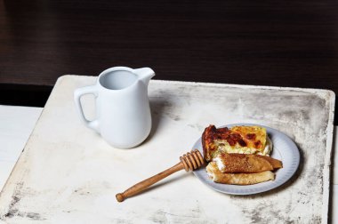 Süzme peynirli ve kuru üzümlü krep ve tabakta süzme peynirli güveç. Mutfak masasında lezzetli bir tatlı ve süt sürahisi.