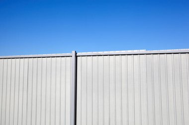 Mavi gökyüzüne karşı yontulmuş çelik çit. Oluklu metal doku yüzeyi veya çeliği galvanize et