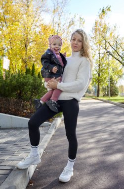 Merhaba Ekim. Anne ve kızı sonbahar şehir parkında yürüyorlar. Ebeveyn ve küçük çocuk dışarıda eğleniyor.