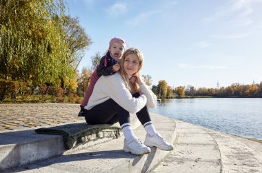 Merhaba Ekim. Anne ve kızı sonbahar şehir parkında yürüyorlar. Ebeveyn ve küçük çocuk dışarıda eğleniyor.