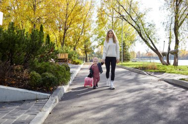 Merhaba Ekim. Anne ve kızı sonbahar şehir parkında yürüyorlar. Ebeveyn ve küçük çocuk dışarıda eğleniyor.