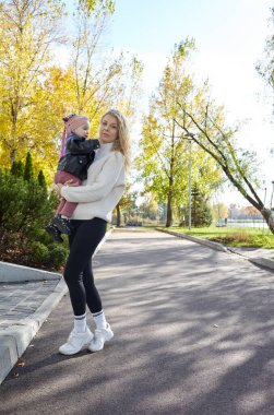 Merhaba Ekim. Anne ve kızı sonbahar şehir parkında yürüyorlar. Ebeveyn ve küçük çocuk dışarıda eğleniyor.