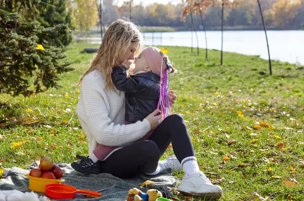 Merhaba Ekim. Anne ve kızı sonbahar şehir parkında yürüyorlar. Ebeveyn ve küçük çocuk dışarıda eğleniyor.