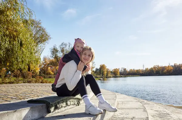 Merhaba Ekim. Anne ve kızı sonbahar şehir parkında yürüyorlar. Ebeveyn ve küçük çocuk dışarıda eğleniyor.